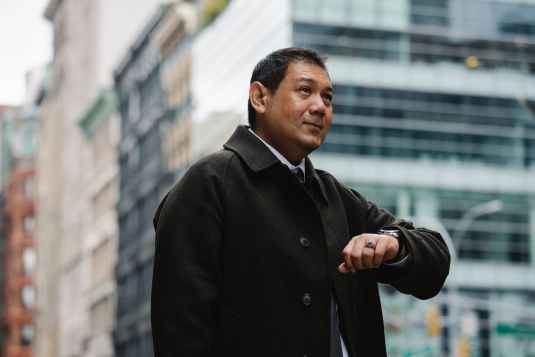 elegant ethnic businessman checking time on wristwatch on city street