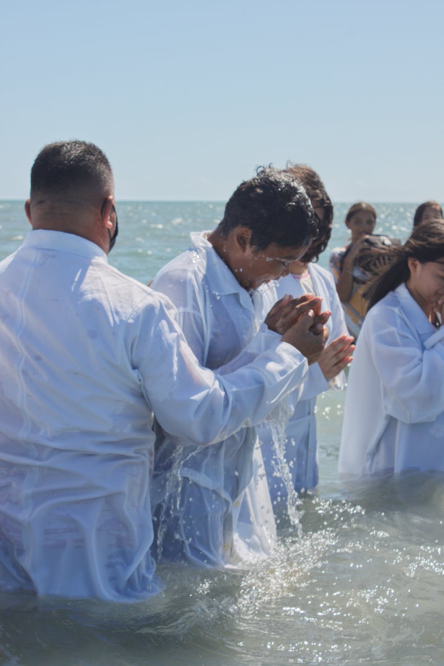 people wearing white shirts getting baptized in a sea